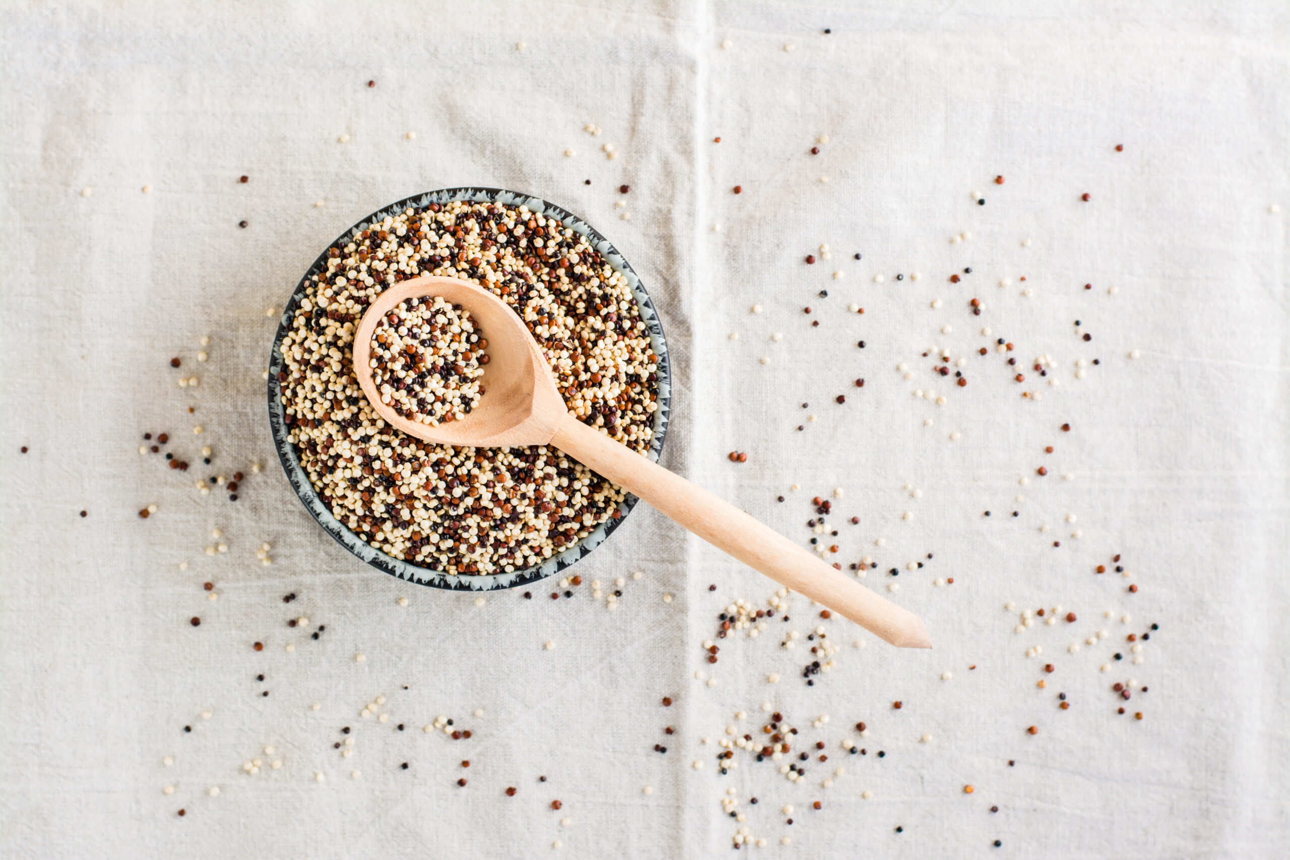 Mix of raw white, red and black quinoa and a wooden spoon in a bowl on a cloth. Healthy gluten free food. Top view